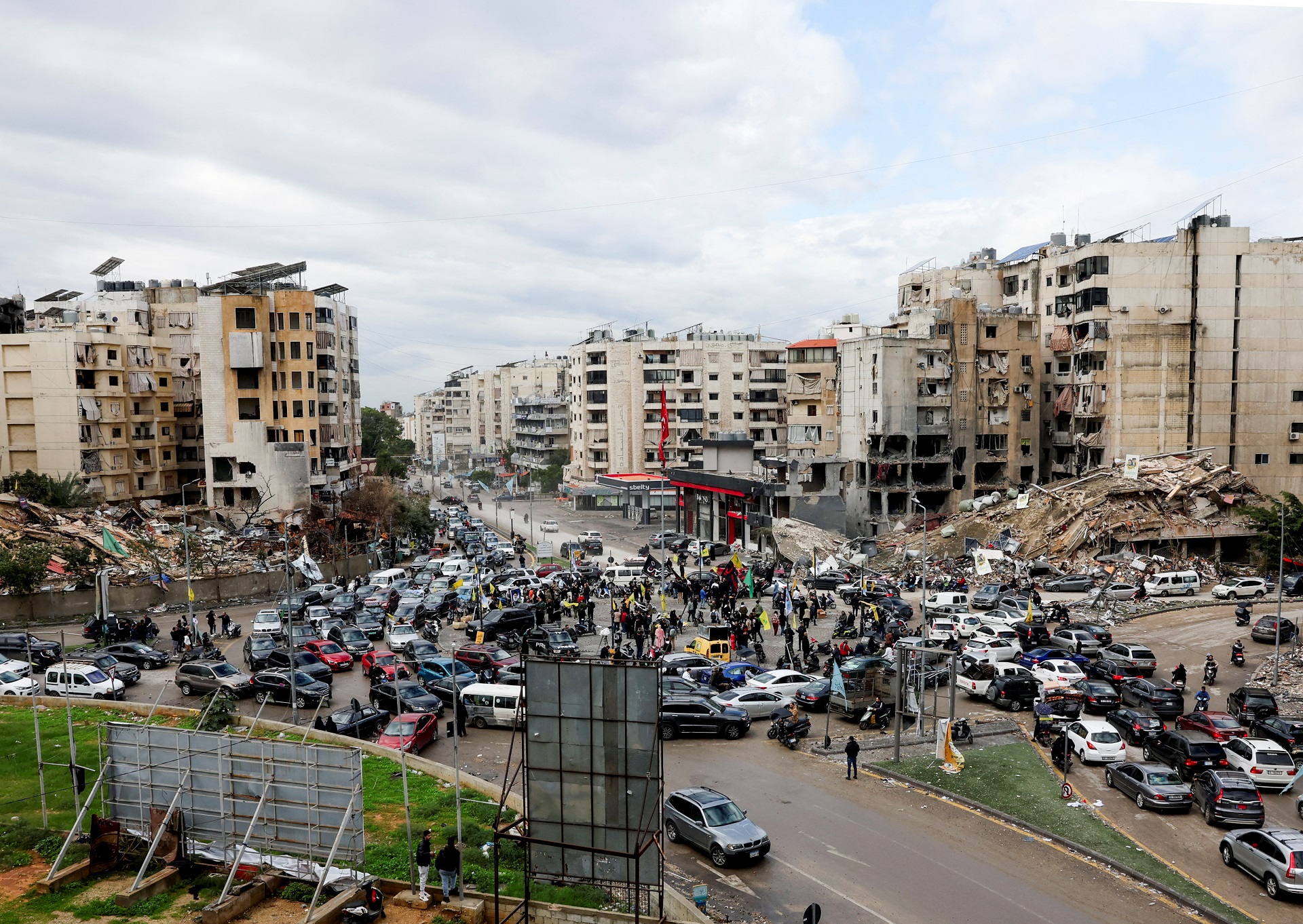 Indivíduos se encontram enquanto automóveis transitam próximos a edifícios afetados, nos arredores ao sul de Beirute, após um acordo de paz entre Israel e o Hezbollah ser implementado, Líbano, 27 de novembro de 2024. REUTERS/Mohamed Azakir