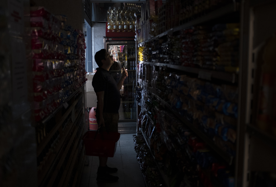 Um cliente utilizando a lanterna do celular em um supermercado